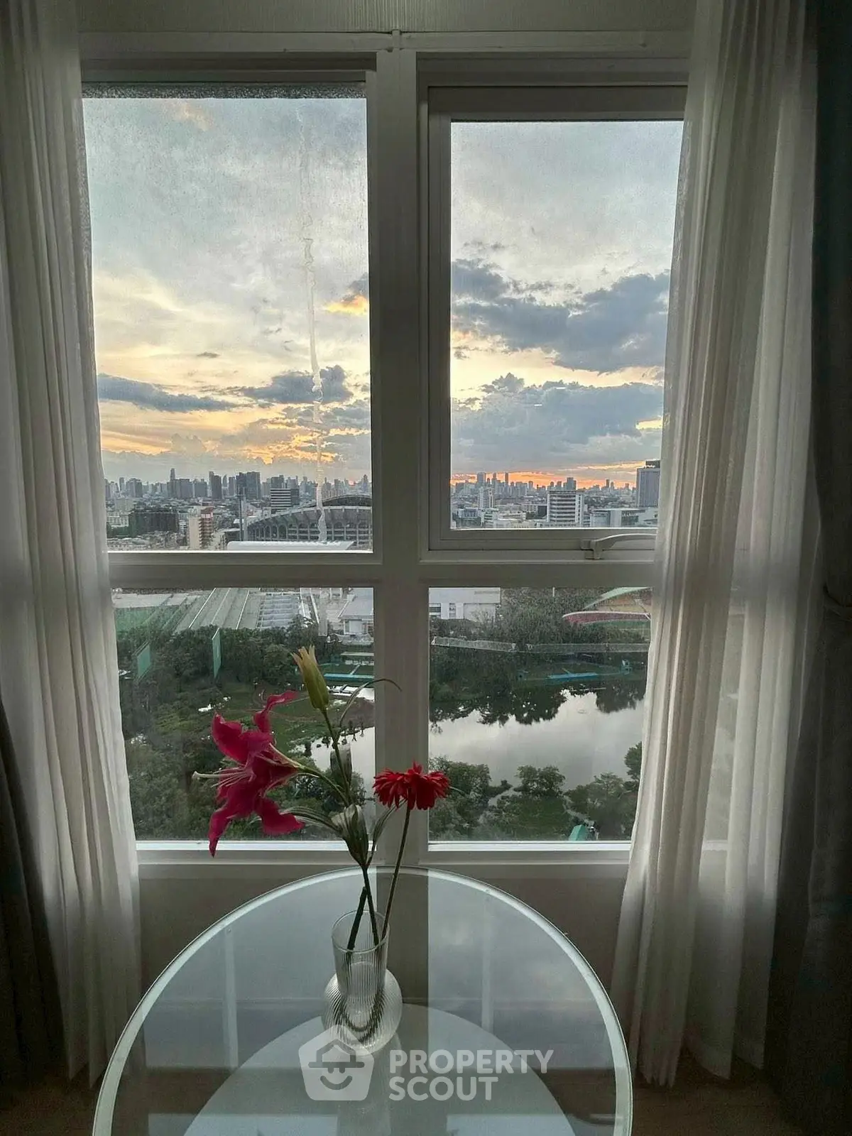 Stunning cityscape view from a window with elegant curtains and a glass table with flowers.