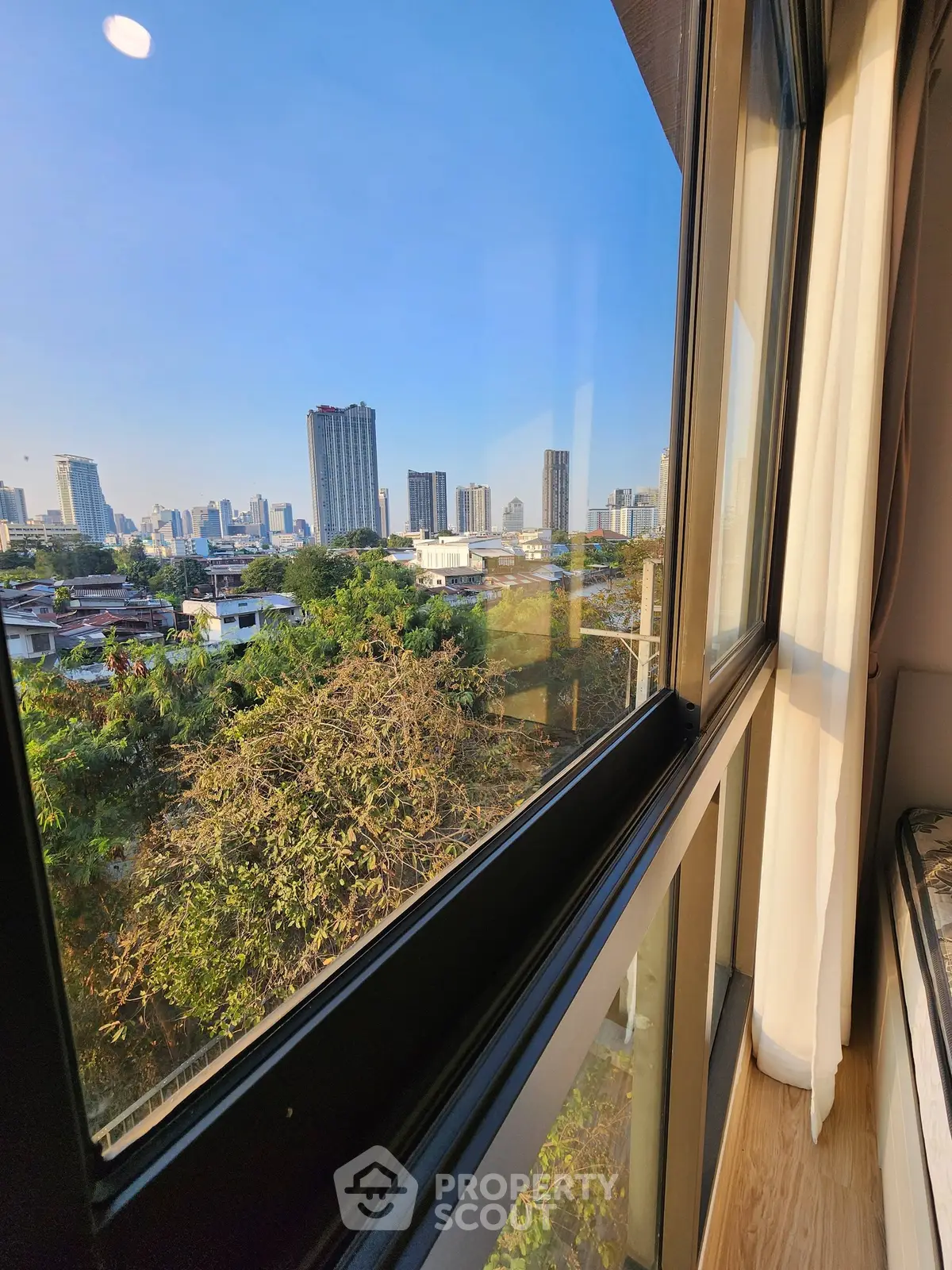Stunning cityscape view from modern apartment window with lush greenery and skyline.
