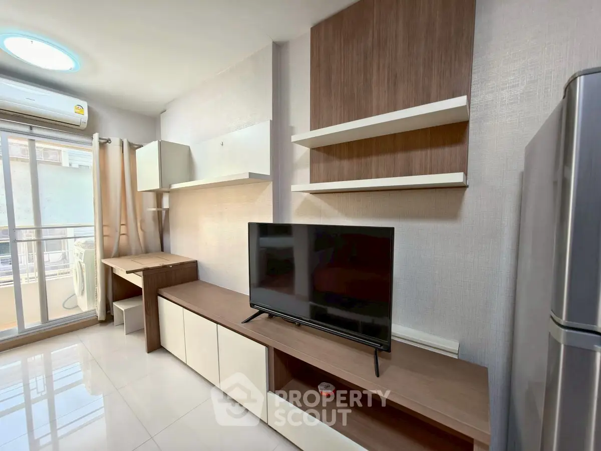 Modern living room with sleek furniture and balcony access, featuring a TV and ample natural light.