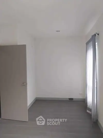 Spacious empty room with gray flooring and natural light from window, ideal for customization.