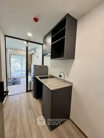 Modern compact kitchen with sleek cabinetry and open layout leading to a bright living area with balcony view.