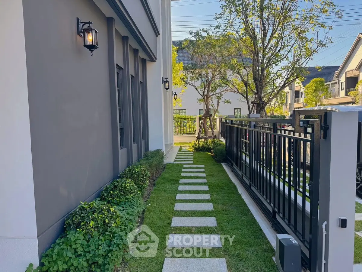 Charming garden pathway with lush greenery and modern fence in a residential area.