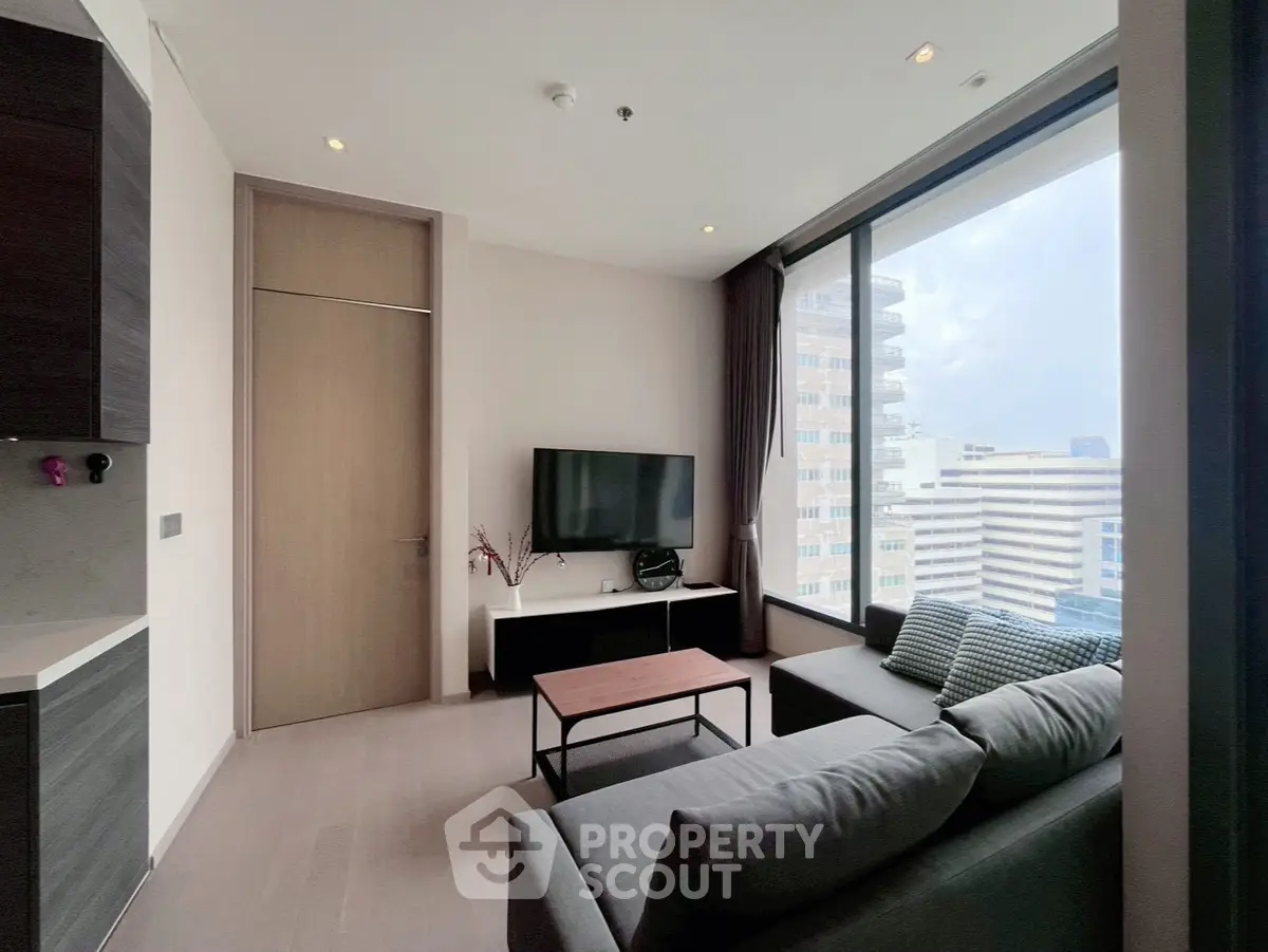 Modern living room with large window and city view, featuring sleek furniture and a mounted TV.