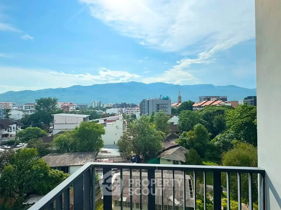 Stunning balcony view overlooking lush greenery and cityscape with mountains in the background.
