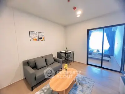 Modern living room with cozy sofa and dining area, leading to a bright bedroom through glass doors.