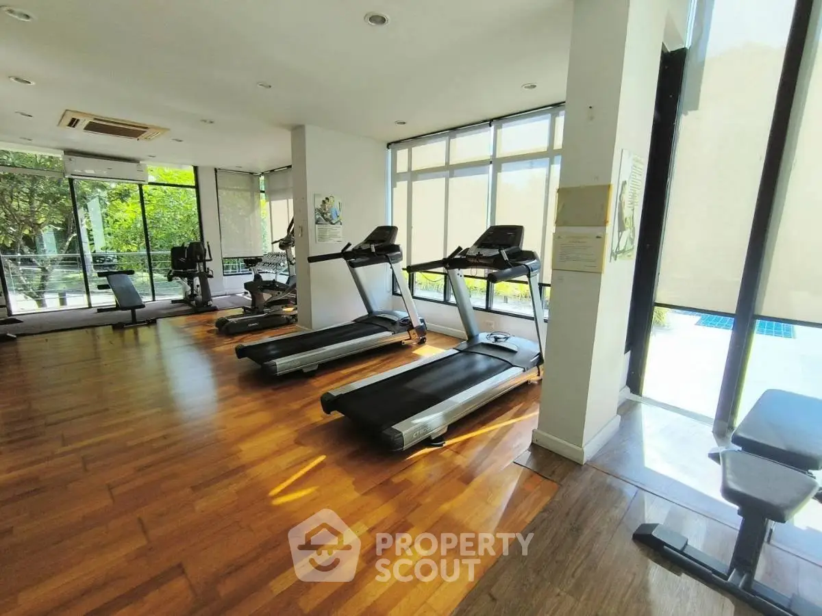 Spacious gym with modern equipment and large windows offering natural light.