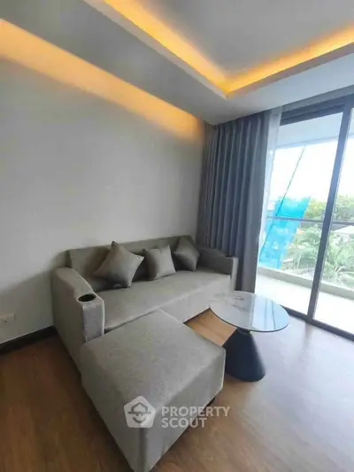 Modern living room with stylish sofa and glass coffee table, featuring large windows and elegant lighting.