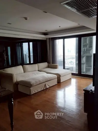 Spacious living room with large windows and city view, featuring a comfortable sectional sofa.