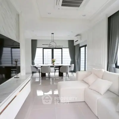 Elegant modern living room with dining area, featuring sleek white decor and large windows.