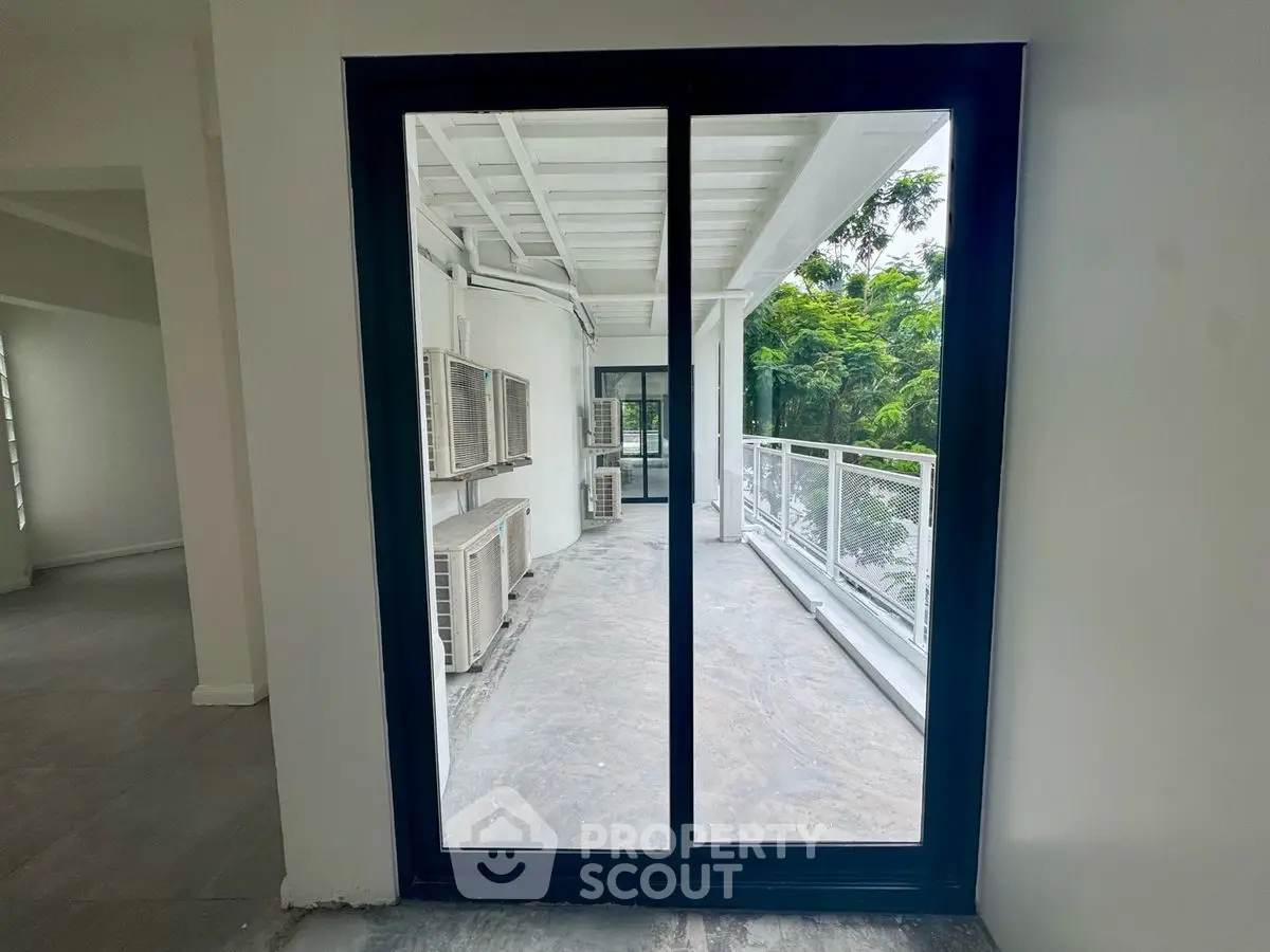 Spacious balcony with sliding glass doors and lush greenery view.