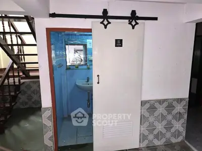 Compact bathroom with sliding door under staircase, featuring blue tiles and a small sink.