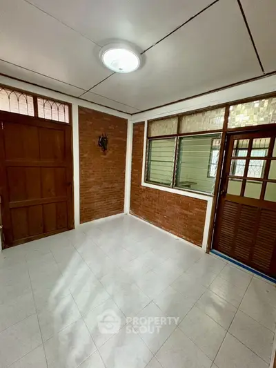 Spacious tiled room with brick accents and wooden doors, ideal for versatile use.