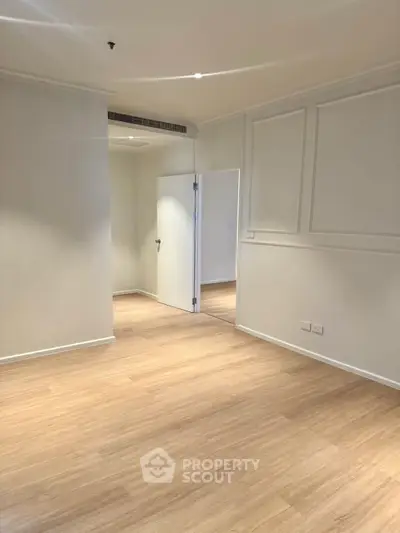Spacious empty room with wooden flooring and white walls, perfect for customization.