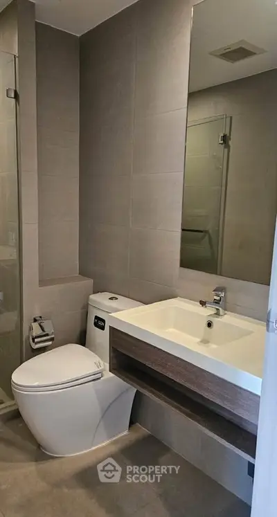 Modern bathroom with sleek fixtures and minimalist design, featuring a glass shower and contemporary sink.