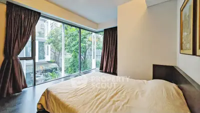 Spacious bedroom with large windows overlooking a lush garden, offering serene views and natural light.