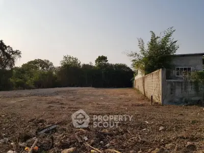Spacious vacant land with potential for development, surrounded by greenery and partial fencing.