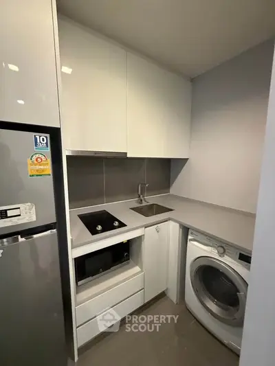 Modern compact kitchen with sleek appliances and washing machine in a stylish apartment.