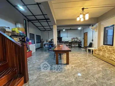 Spacious open-plan living area with modern lighting and tiled flooring, featuring a long dining table and cozy seating.