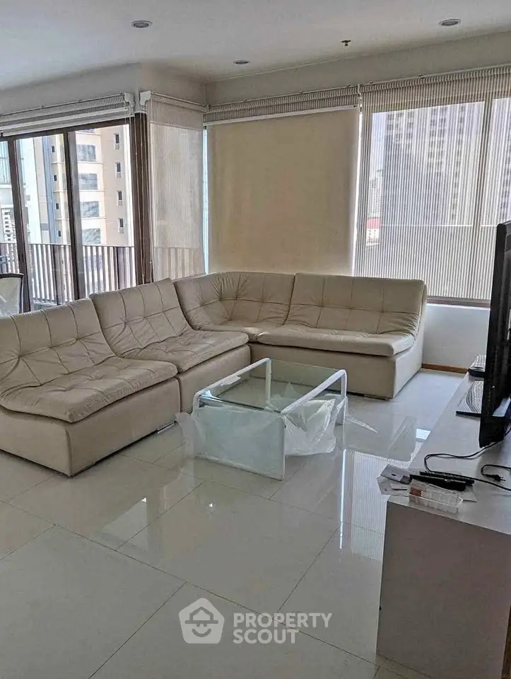 Spacious living room with modern sectional sofa and large windows offering city views.