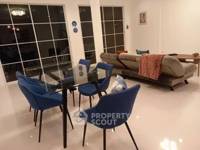 Modern living room with glass dining table and blue chairs, stylish sofa, and elegant decor.