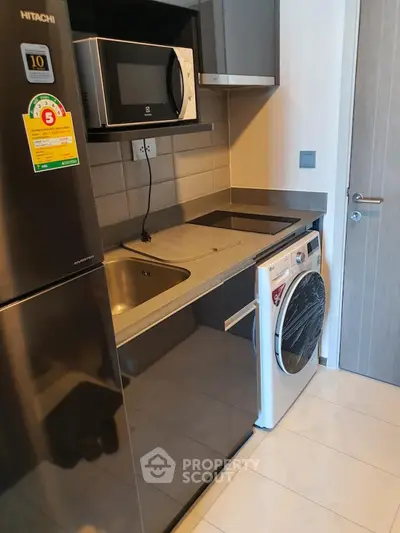 Modern kitchen with sleek appliances including fridge, microwave, and washing machine in compact layout.