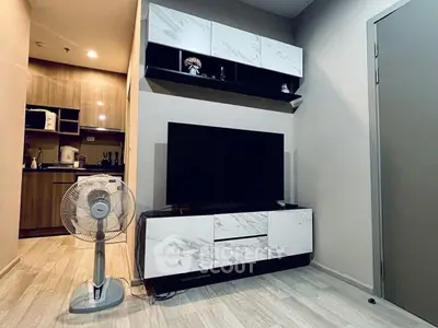 Modern living room with sleek TV stand and fan, adjacent to a compact kitchen area.