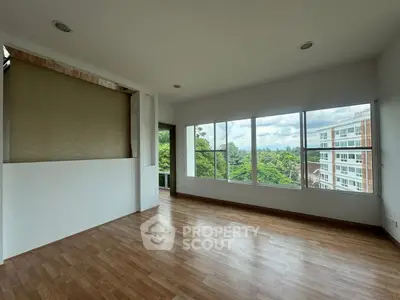 Spacious living room with large windows offering a stunning view of lush greenery and modern buildings.