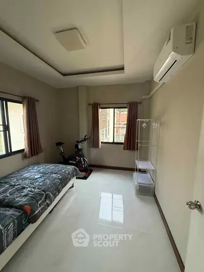 Cozy bedroom with modern decor and exercise bike, featuring air conditioning and ample natural light.