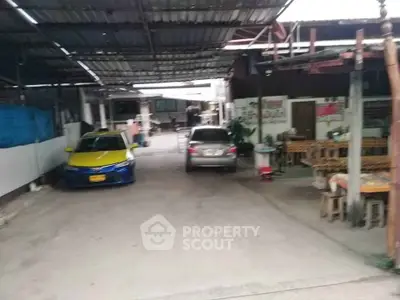 Outdoor parking area with two cars and adjacent seating area under a metal roof.