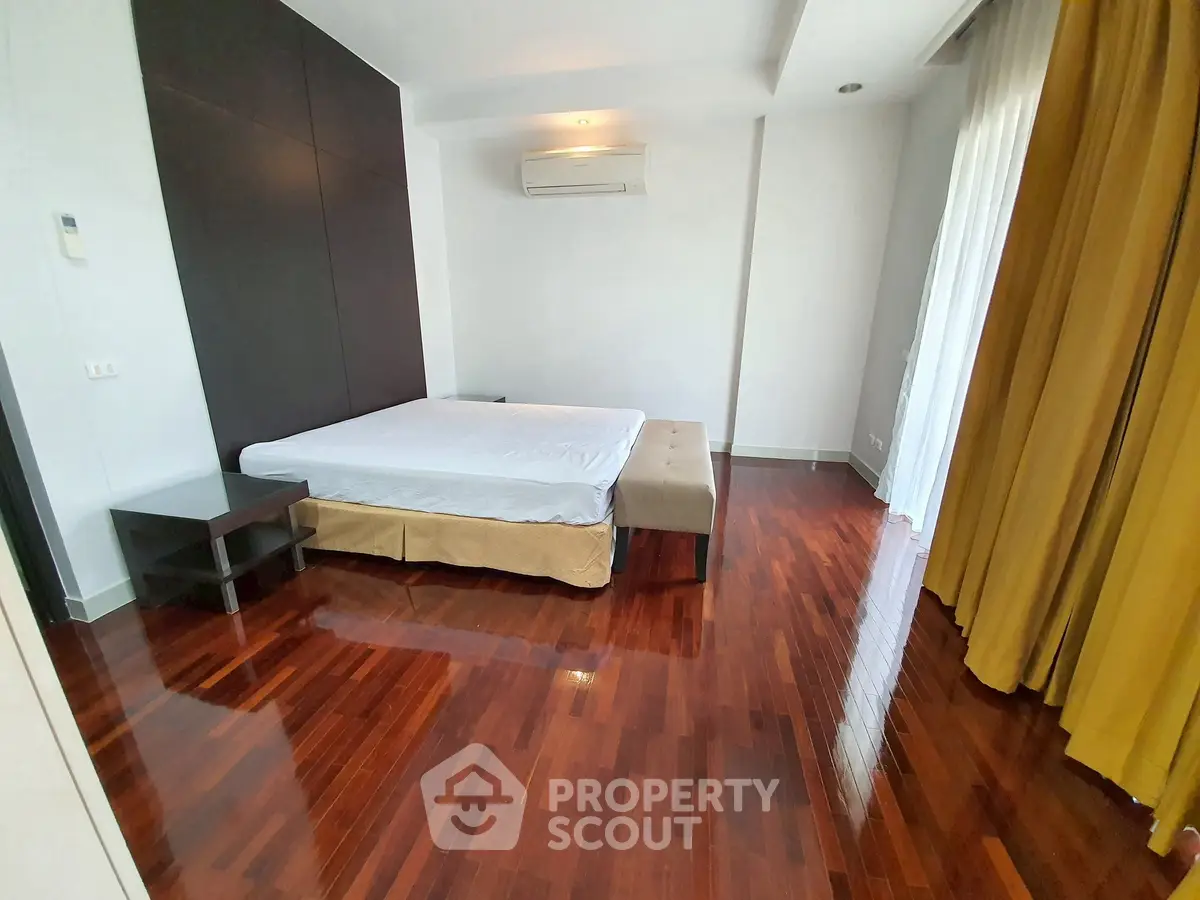 Spacious bedroom with polished wooden floors and modern furnishings in a luxurious apartment.