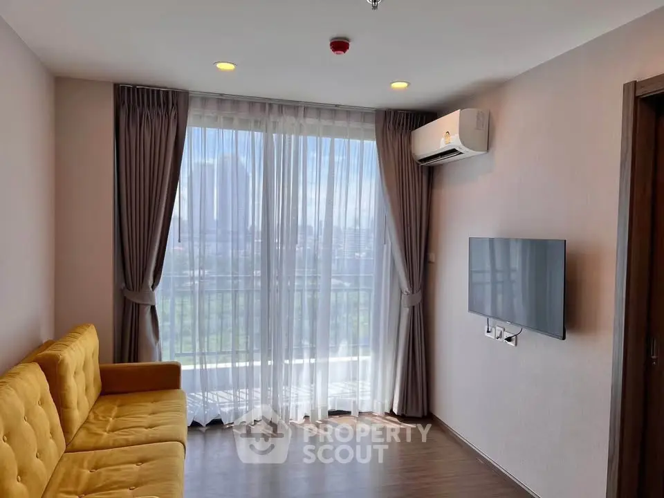 Modern living room with yellow sofa, wall-mounted TV, and city view through large window.