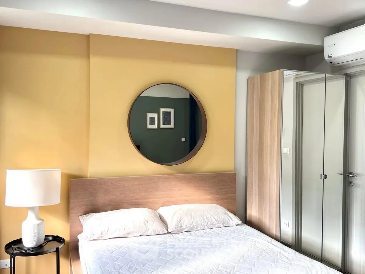 Modern bedroom with stylish decor, featuring a round mirror, cozy bed, and air conditioning for comfort.