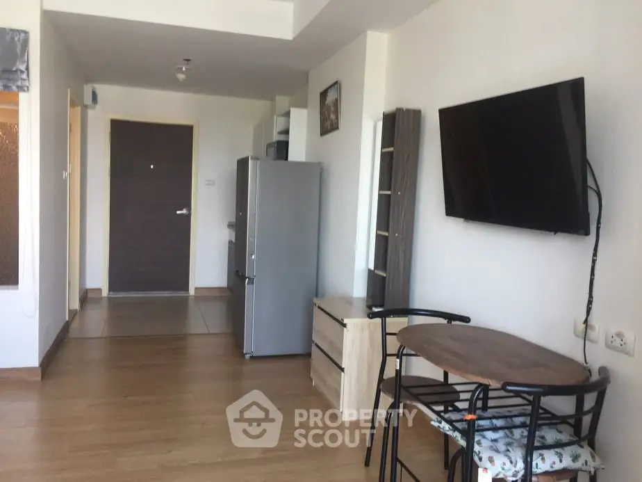 Modern apartment interior with wall-mounted TV, dining set, and sleek kitchen appliances.