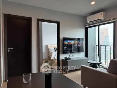 Modern living room with balcony and city view, featuring sleek furniture and wall-mounted TV.