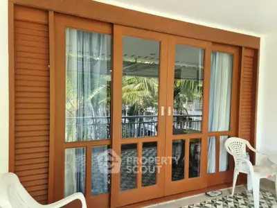 Elegant wooden sliding doors open to a tropical balcony with lush greenery view