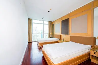 Spacious bedroom with two beds and city view, featuring elegant wooden flooring and large windows.