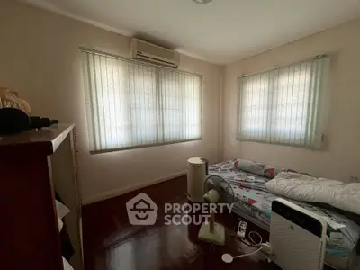 Cozy bedroom with air conditioning and natural light, featuring a simple bed and wooden flooring.