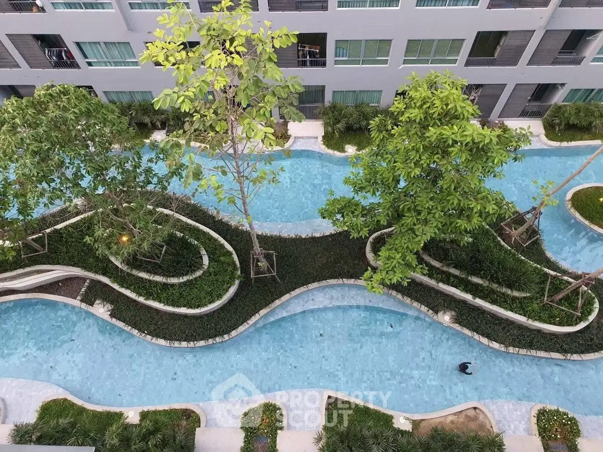 Stunning aerial view of modern apartment complex with winding pool and lush greenery.