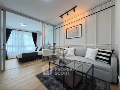 Modern living room with stylish decor and cozy seating area, adjacent to a bright bedroom with large windows.