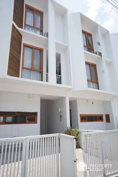 Modern white townhouse with wooden accents and gated entrance, featuring large windows and a minimalist design.