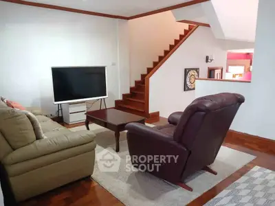 Cozy living room with modern TV and comfortable seating near wooden staircase.