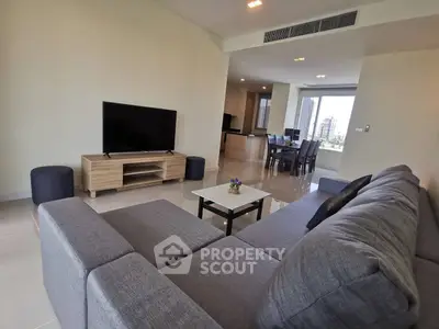Spacious living room with modern gray sofa and large TV, open layout to dining area.