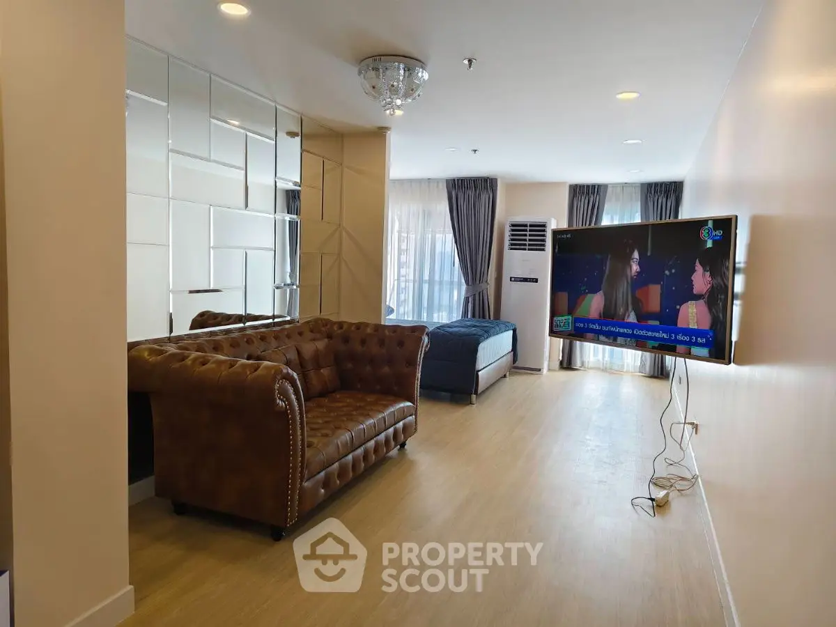 Spacious living room with elegant leather sofa and wall-mounted TV, featuring modern decor and ample natural light.