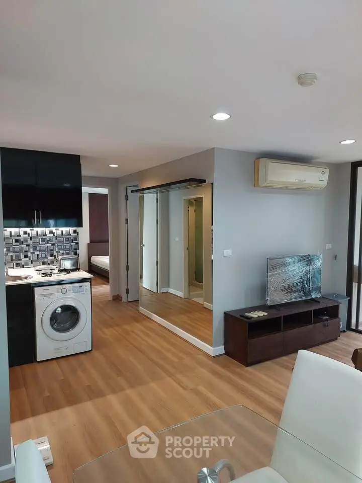 Modern open-plan living room with sleek kitchen and washing machine, featuring stylish decor and ample natural light.