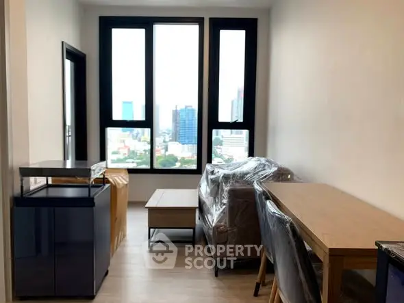 Modern living room with large windows and city view, featuring sleek furniture and natural light.