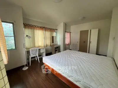 Spacious bedroom with wooden flooring and natural light, featuring a large bed and study desk.