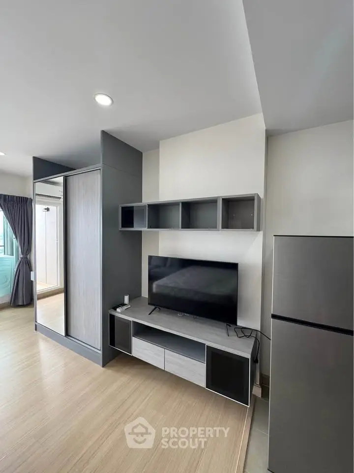 Modern living room with sleek TV stand and large fridge, featuring minimalist design and ample natural light.