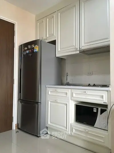 Modern kitchen with sleek appliances and white cabinetry, featuring a fridge and microwave.