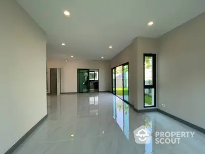 Spacious and modern living area with glossy tiled floors, ample natural light, and a view of the green outdoors through large windows.