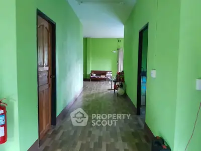 Spacious hallway with vibrant green walls and wooden flooring leading to a cozy living area.